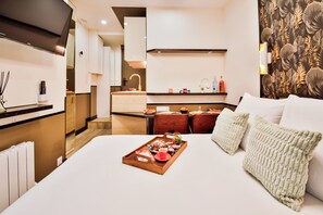 Une chambre d'hôtel moderne avec un grand lit, un plateau en bois contenant des articles pour le petit-déjeuner, un coin cuisine en arrière-plan et un mur à motifs.