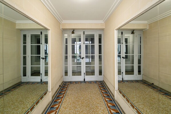 A hallway with a patterned floor, double doors with glass panels, and a light fixture on the ceiling. - WS Champs-Elysées - Daru (Paris)