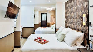 A modern hotel room with a large bed, a flat-screen TV mounted on the wall, a decorative wall panel, and a bedside table with a bottle. - WS Champs-Elysées - Daru (Paris)