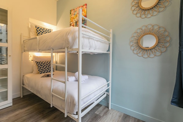 Quarto com beliche, roupa de cama branca, espelho e decoração na parede.