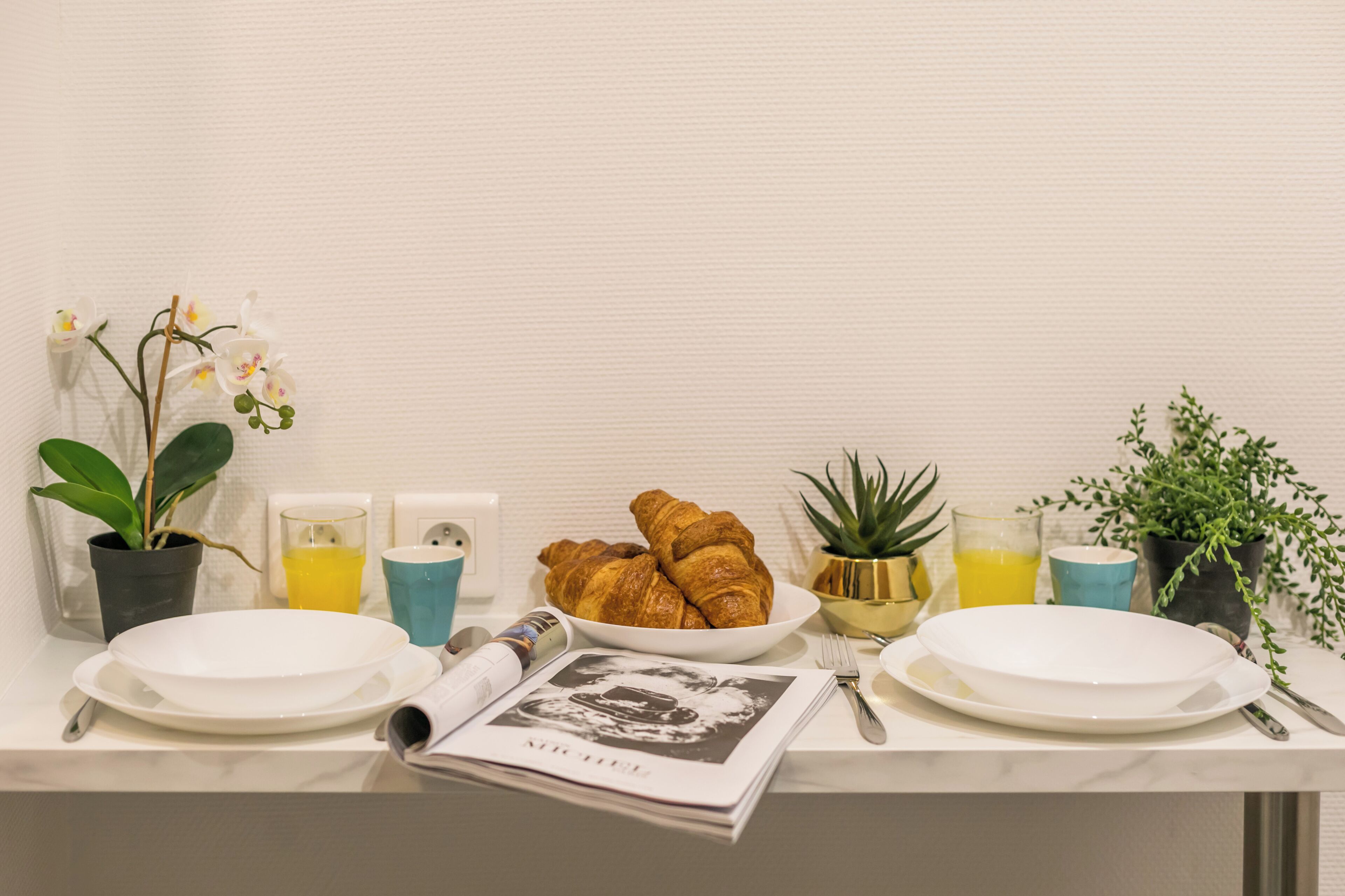 Una mesa de desayuno con cruasanes, un periódico y una planta.
