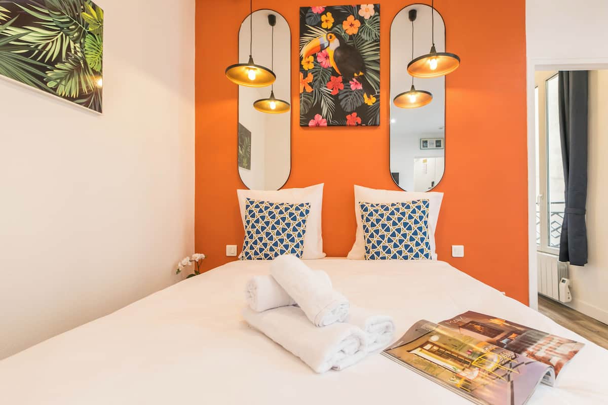 Una habitación de hotel con una cama grande, dos espejos montados en la pared y un cuadro con motivos tropicales.