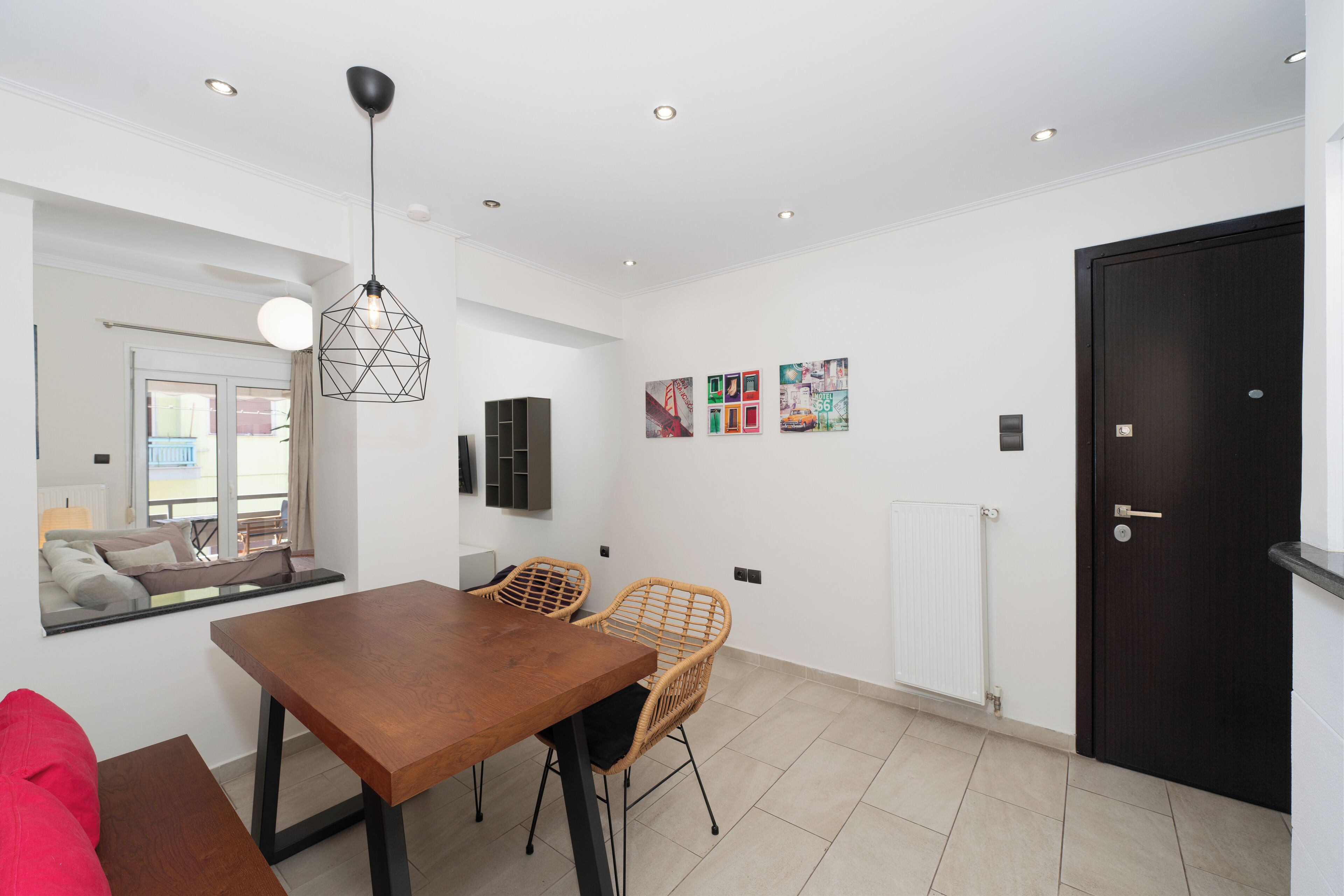 A modern dining area with a wooden table and wicker chairs, a black door, and wall art.