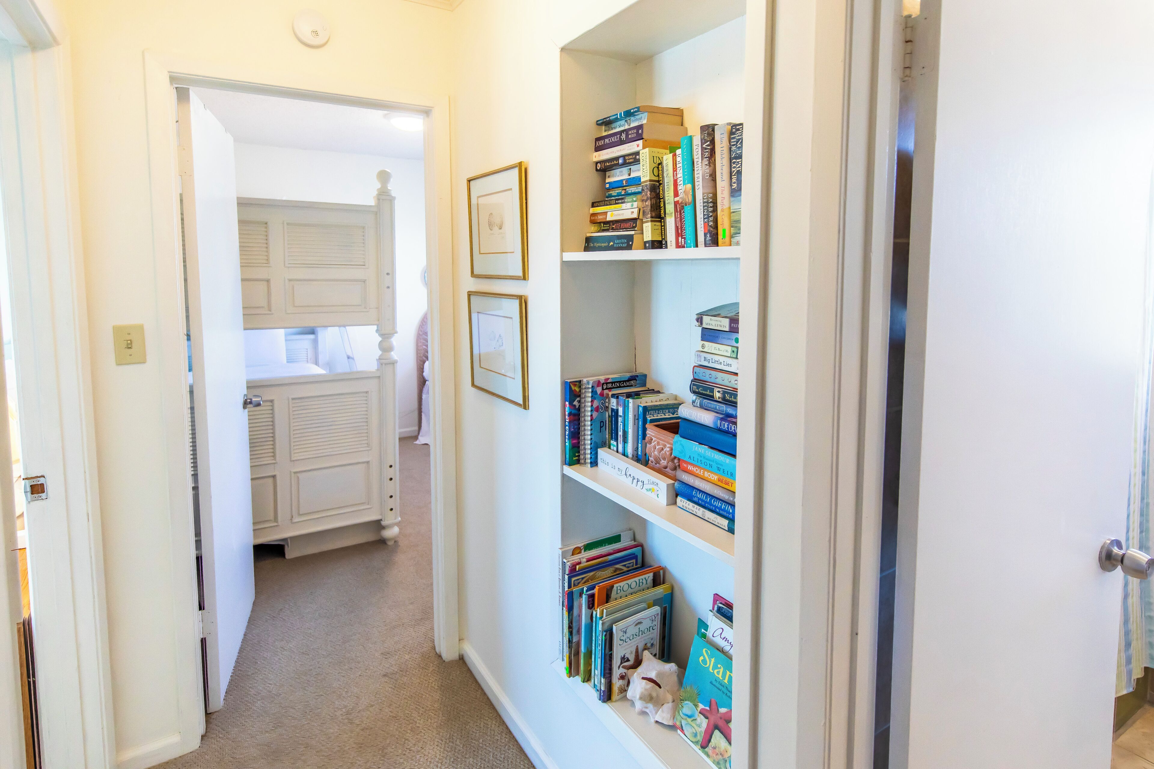 A hallway with a bookshelf filled with books and a door leading to a room with a bed.