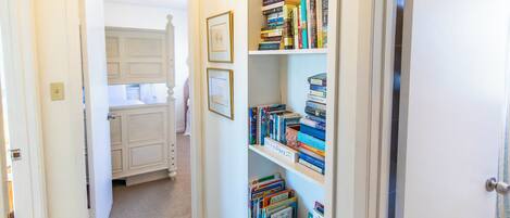 A hallway with a bookshelf filled with books and a door leading to a room with a bed.