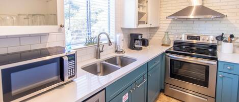 A modern kitchen with stainless steel appliances, a double sink, and teal cabinetry.