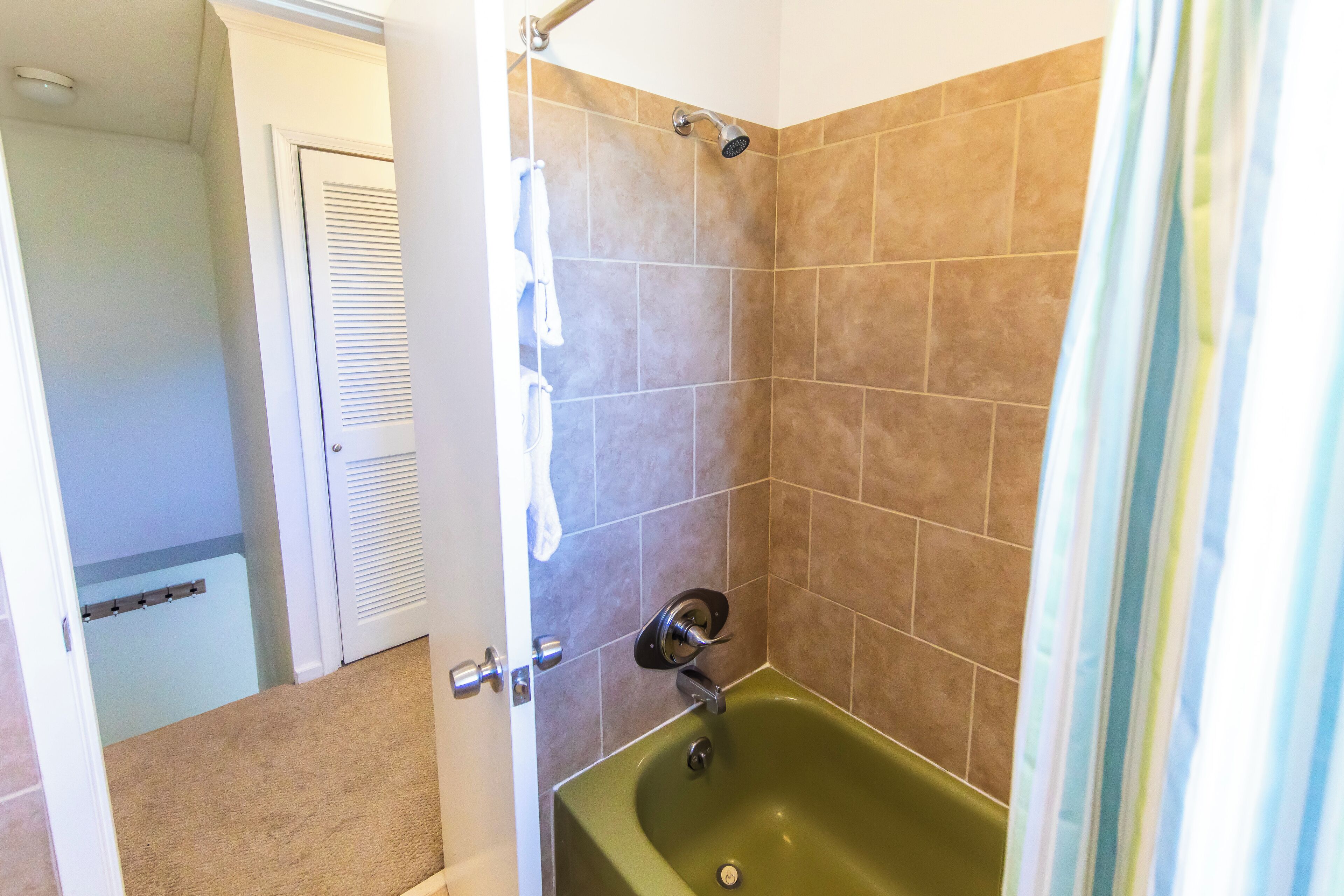 Une salle de bain avec une baignoire verte, des carreaux beiges et une pomme de douche.