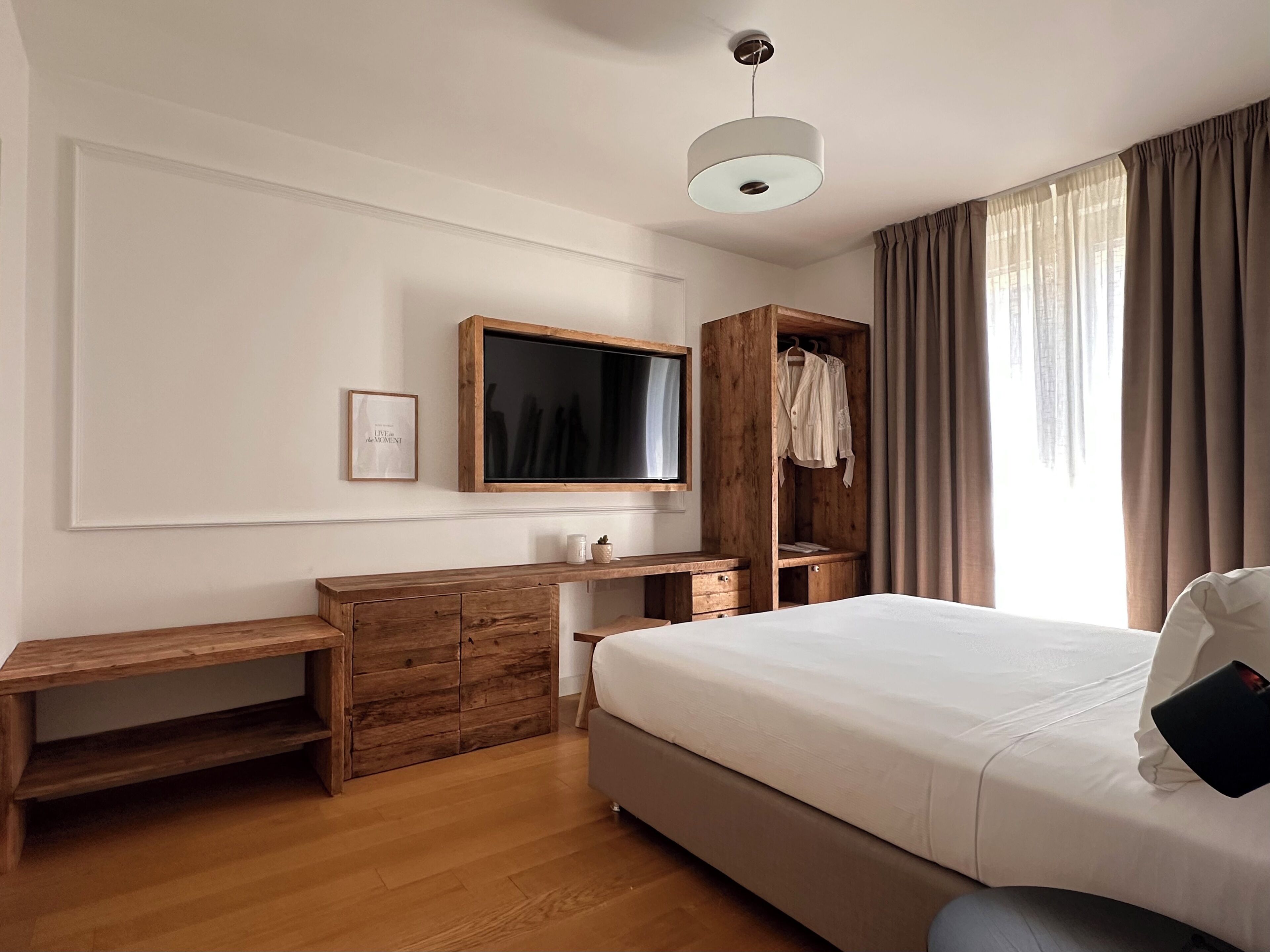 A bedroom with a bed, wooden dresser, desk, and a TV mounted on the wall.