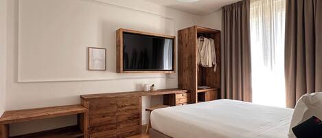A bedroom with a bed, wooden dresser, desk, and a TV mounted on the wall.