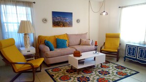A living room with a sofa, two yellow armchairs, a coffee table, a patterned rug, a lamp, a picture on the wall, and a cabinet. - Space Coast Condo in the heart of Titusville (Titusville)