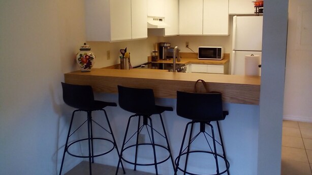 A compact kitchen with a central island, three bar stools, a ceiling fan, and basic appliances. - Space Coast Condo in the heart of Titusville (Titusville)