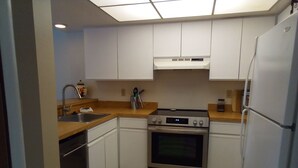 A compact kitchen with white cabinets, a stainless steel oven, a refrigerator, and a wooden countertop. - Space Coast Condo in the heart of Titusville (Titusville)