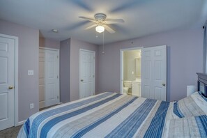 Ein Schlafzimmer mit Bett, Deckenventilator und einem durchgehenden Türrahmen sichtbarem Badezimmer.