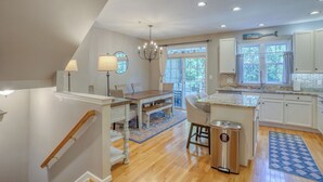 A spacious kitchen with a central island, a dining area with a chandelier, and a view through large windows. - Spacious 4-bed 3.5-bath Townhome in Long Neck with AC, Swimming Pool & Game Room (Long Neck)
