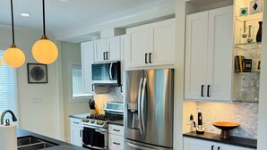 A modern kitchen with white cabinets, stainless steel appliances, and pendant lighting. - NEW! Charming Pet Friendly Modern Cottage in the Historic District of Saugatuck! (Saugatuck)