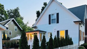 A two-story house with a white picket fence, a well-maintained lawn, and a patio area with outdoor furniture. - NEW! Charming Pet Friendly Modern Cottage in the Historic District of Saugatuck! (Saugatuck)