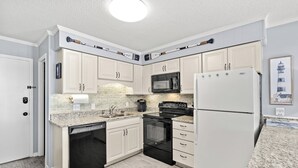 A modern kitchen with white cabinets, a granite countertop, a built-in oven, a microwave, and a refrigerator.