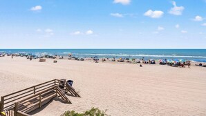 A beach with a wooden boardwalk leading to the water, umbrellas, and people.