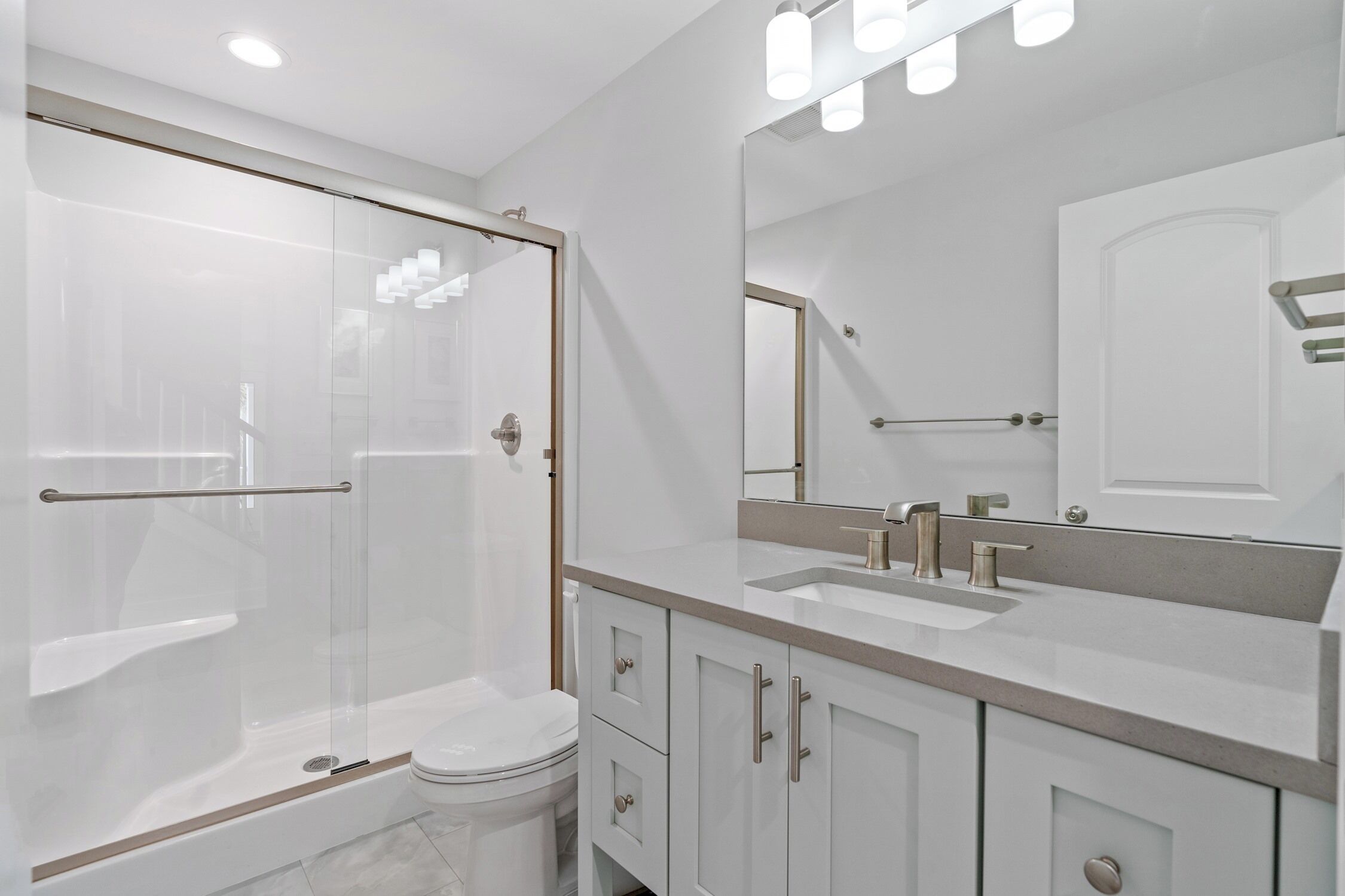 Un baño moderno con ducha envuelta en vidrio, inodoro y tocador con un espejo grande.