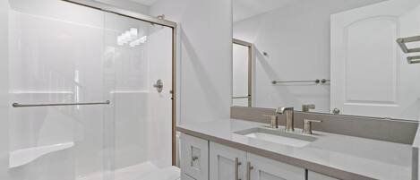 Un baño moderno con ducha envuelta en vidrio, inodoro y tocador con un espejo grande.