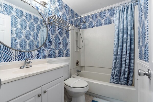 A bathroom with a white sink, toilet, and bathtub. The walls have a blue leaf pattern. - Cross Street to Beach - Waipani D3 - 1st Floor (North Myrtle Beach)