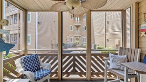 A covered outdoor seating area with wicker furniture, a ceiling fan, and a view of adjacent buildings.