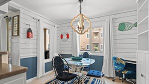 A dining area with a round table, chairs, and a chandelier. There are life rings on the wall and a fish decoration.