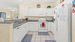 Une cuisine moderne avec des meubles blancs, un four à micro-ondes, un four et un réfrigérateur. Deux tapis à motifs bleus sont posés sur le sol.