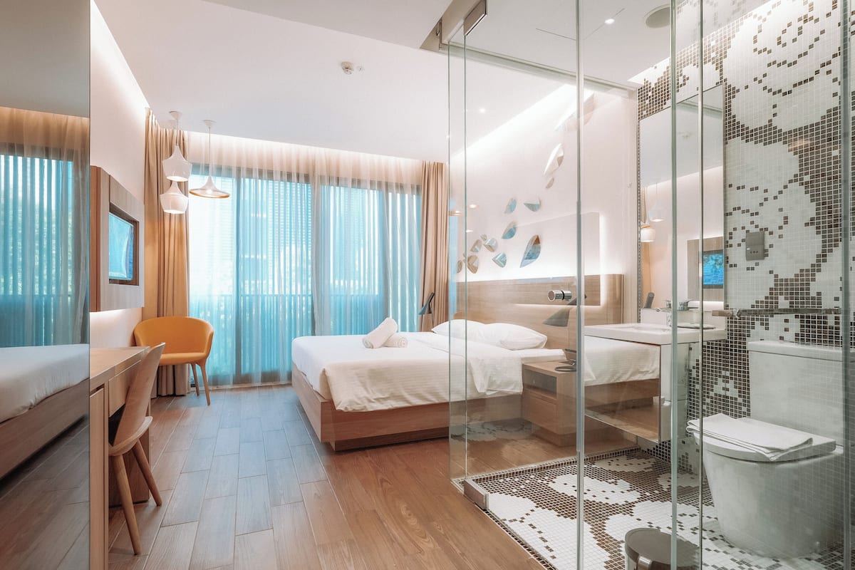 Quarto de hotel moderno com uma cama, escrivaninha e área de chuveiro.
