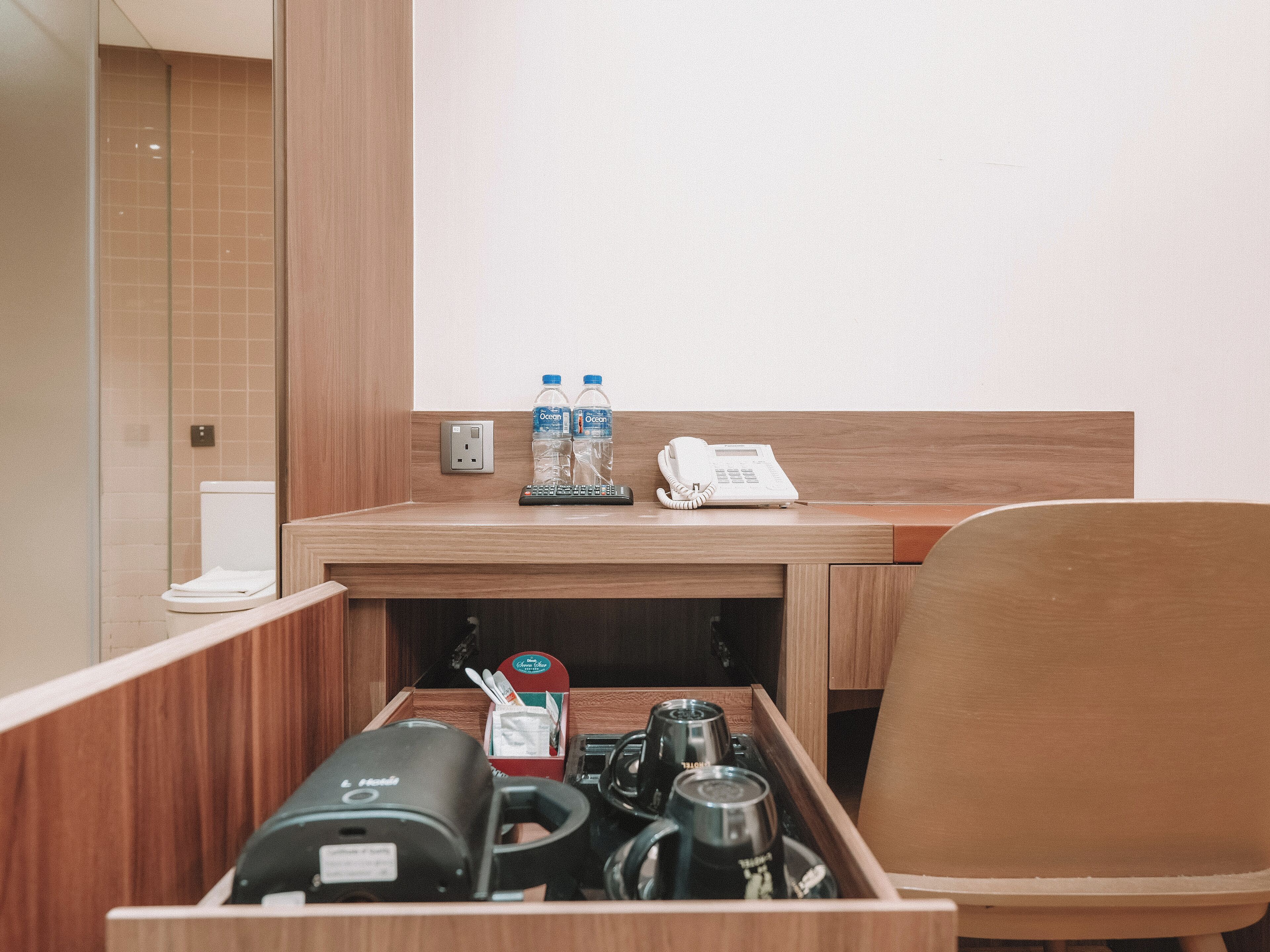 A hotel room with a wooden desk, a telephone, two bottles of water, and a coffee maker.