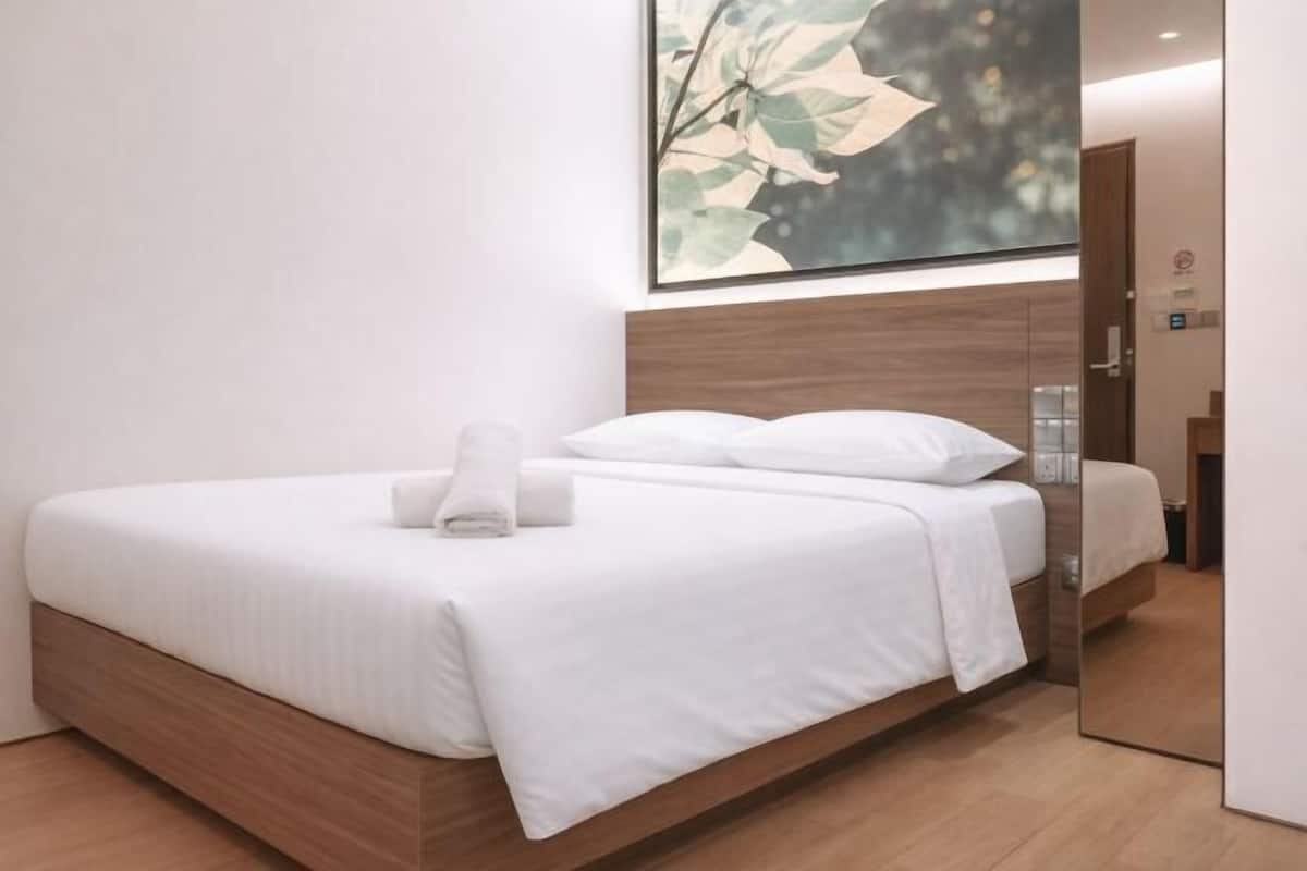 Quarto de hotel moderno com estrutura de cama de madeira, roupa de cama branca, um espelho grande e uma obra de arte na parede.