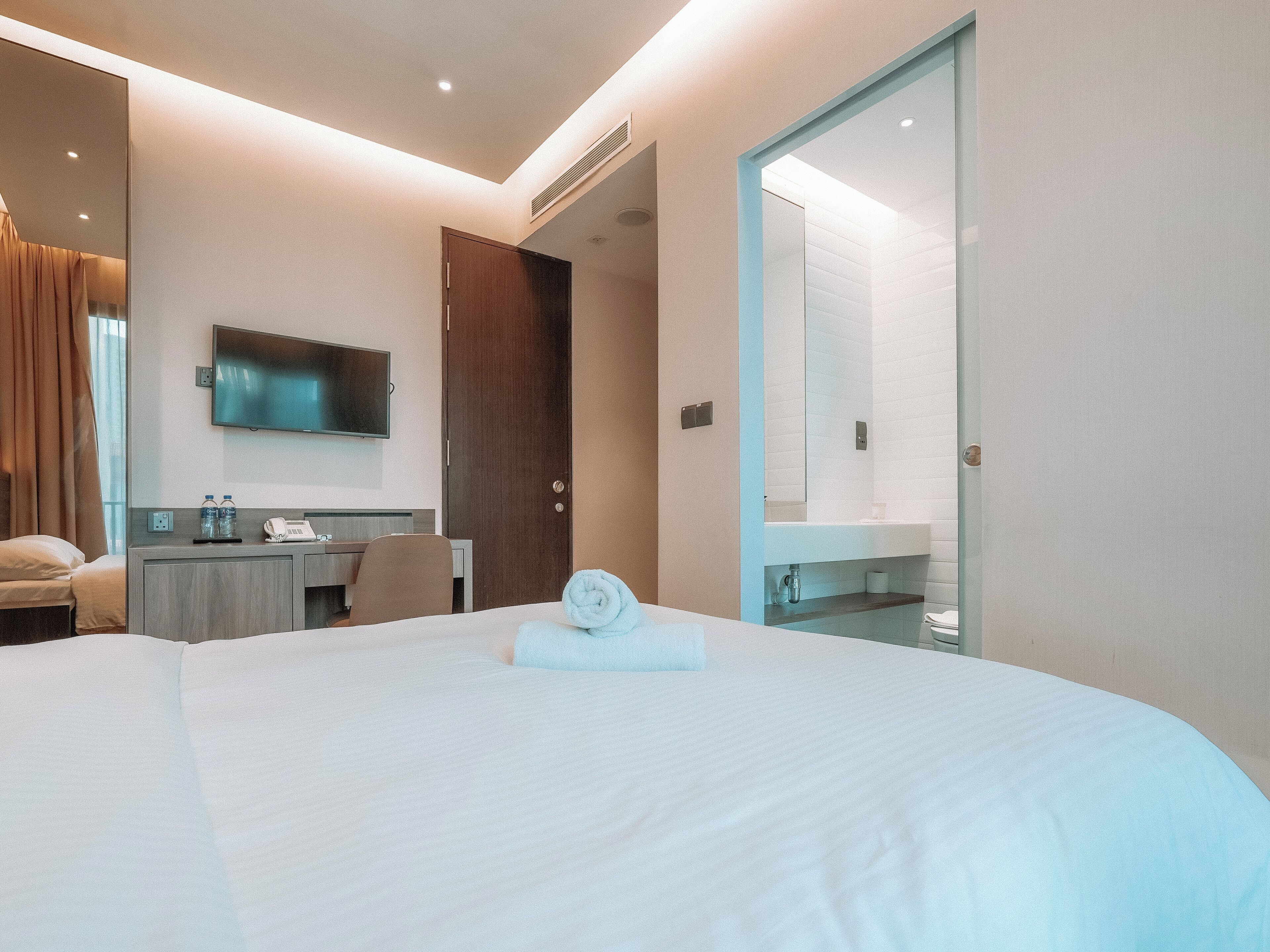 A modern hotel room with a large bed, a desk, a flat-screen TV, and a bathroom with a glass partition.