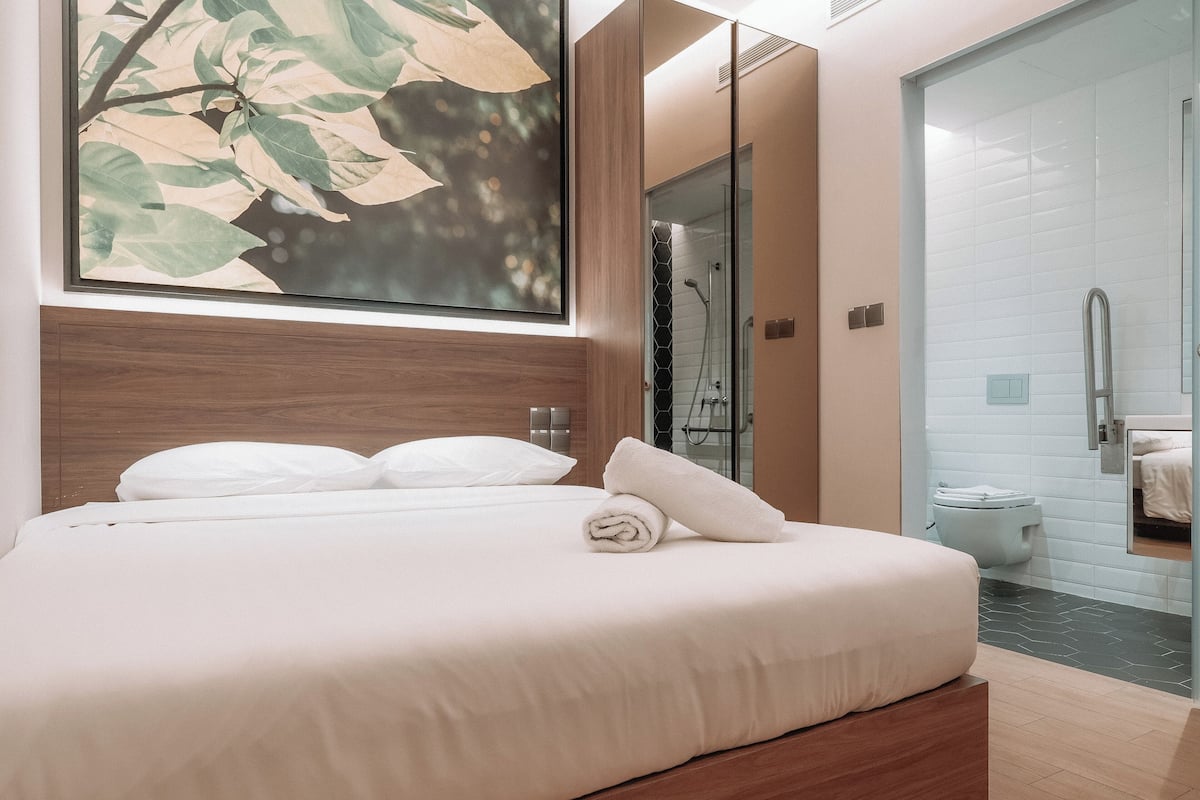 Quarto de hotel moderno com uma cama grande, chuveiro envidraçado e vista para o banheiro.