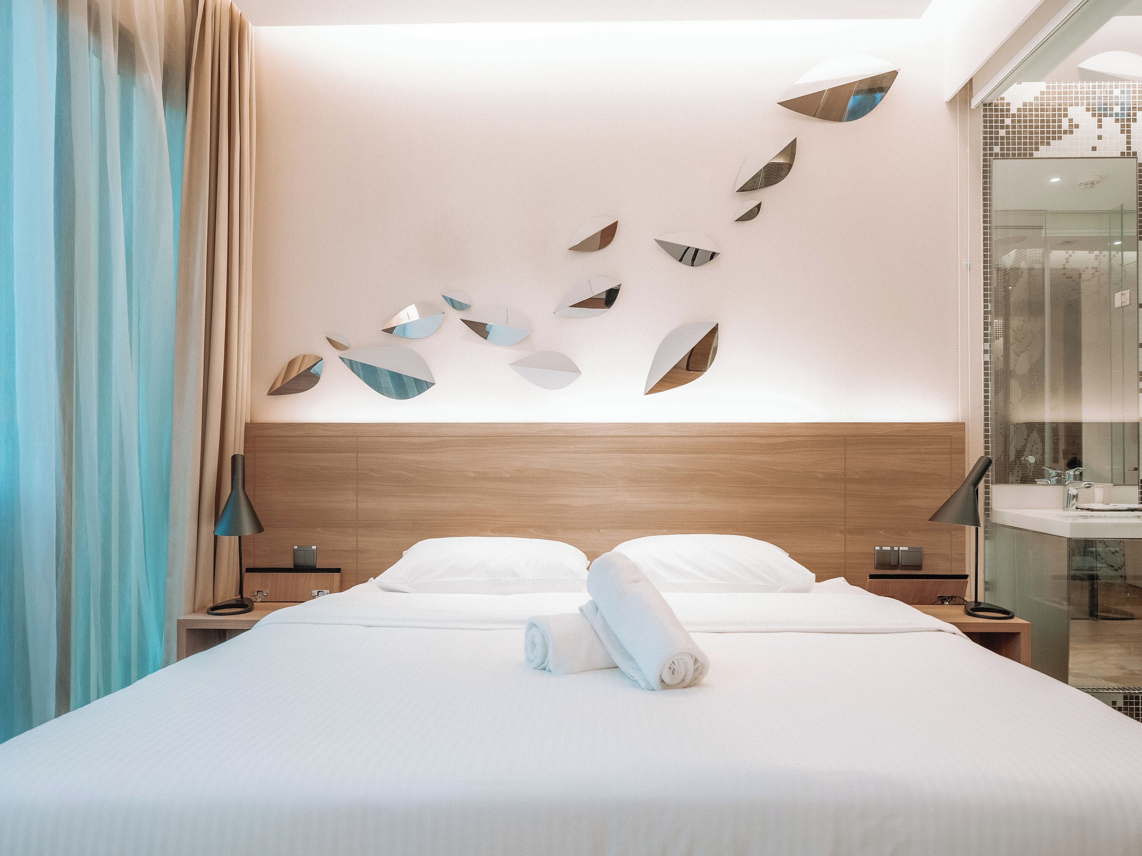 Une chambre d’hôtel moderne avec un lit bien fait, une tête de lit en bois et un mur orné d’œuvres d’art abstraites.