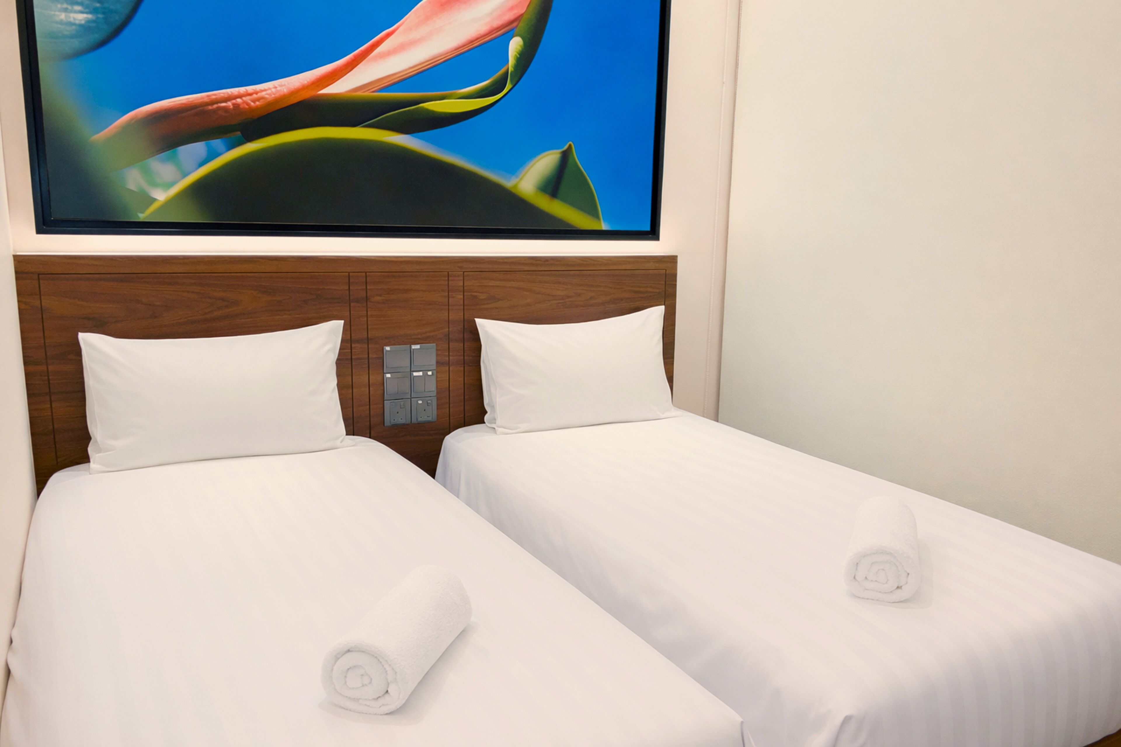 Una camera d'albergo con due letti singoli, lenzuola bianche e un quadro grande sopra la testiera.