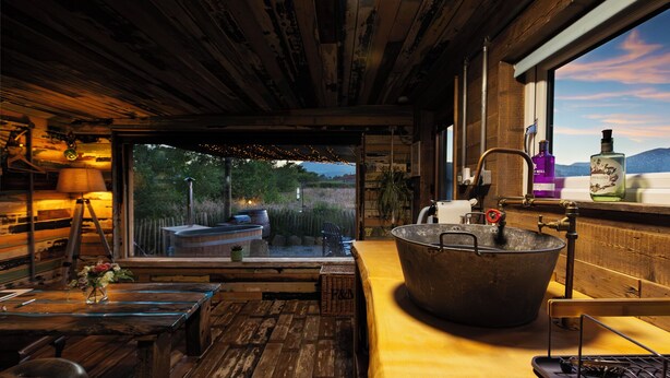 A rustic cabin interior with a wooden floor, a large metal sink, a window with a view of the outdoors, and a wooden bench. - Romantic Rural Retreat - Rustic Cabin in the Mournes with Private Hot Tub (Annalong)
