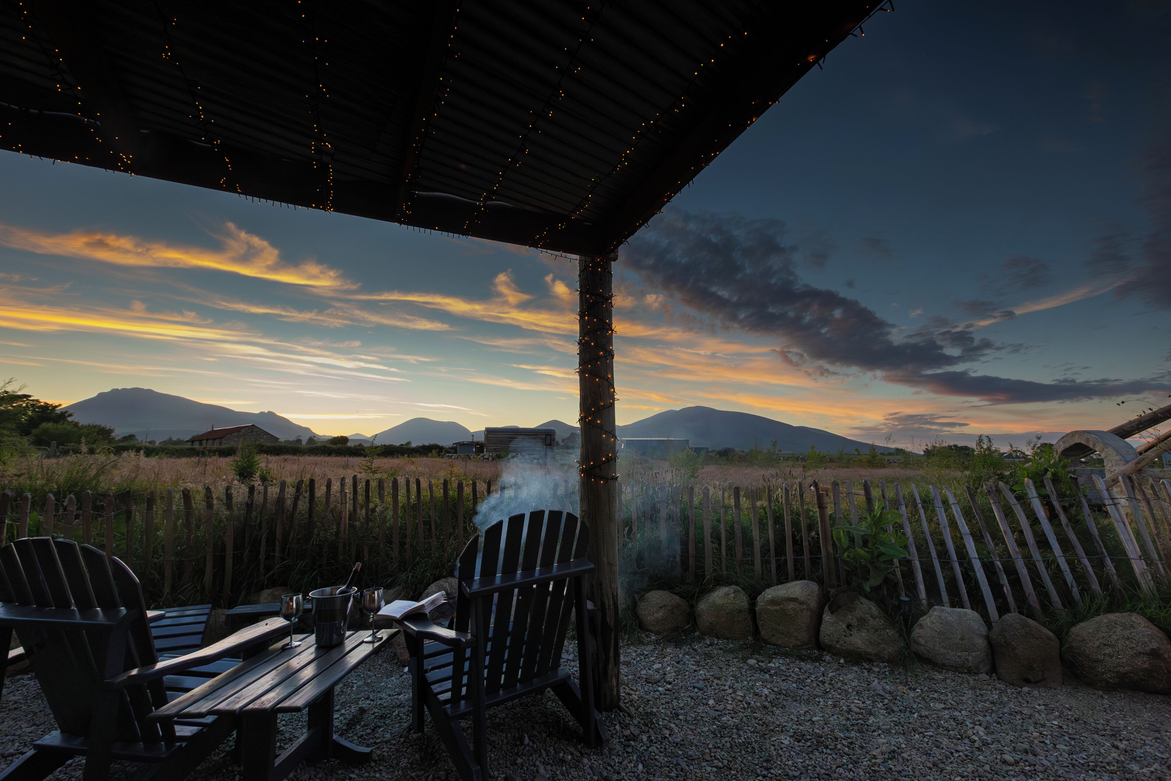 An outdoor seating area with chairs and a table, overlooking a field with mountains in the distance.