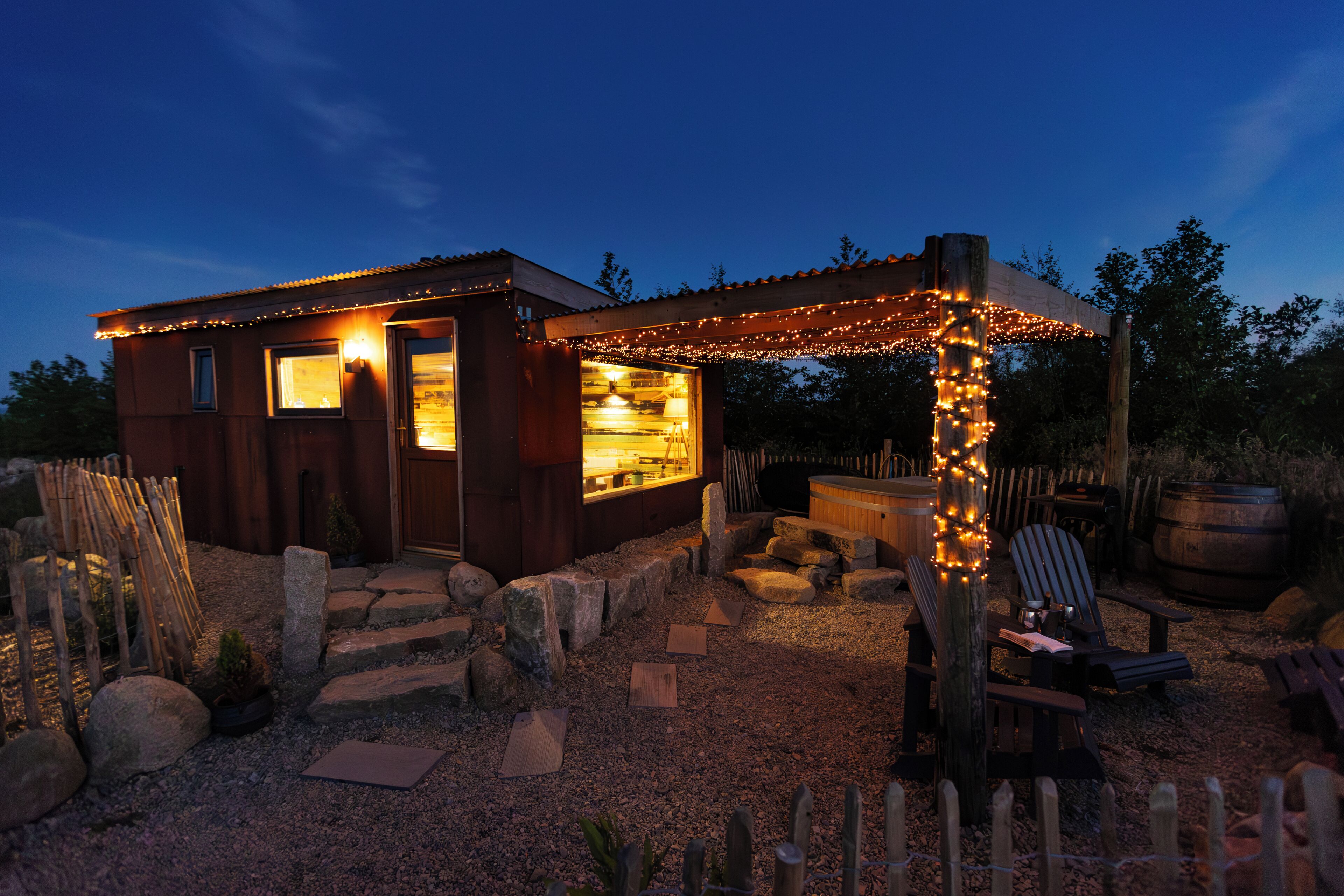 A rustic cabin with a wooden exterior, a covered outdoor seating area, and a gravel pathway leading to the entrance.