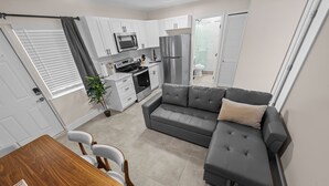 A compact kitchen with white cabinets, a grey sofa, and a dining table with chairs. - Relaxing 2-Bedroom Apartment w / Pool Access (Fort Lauderdale)