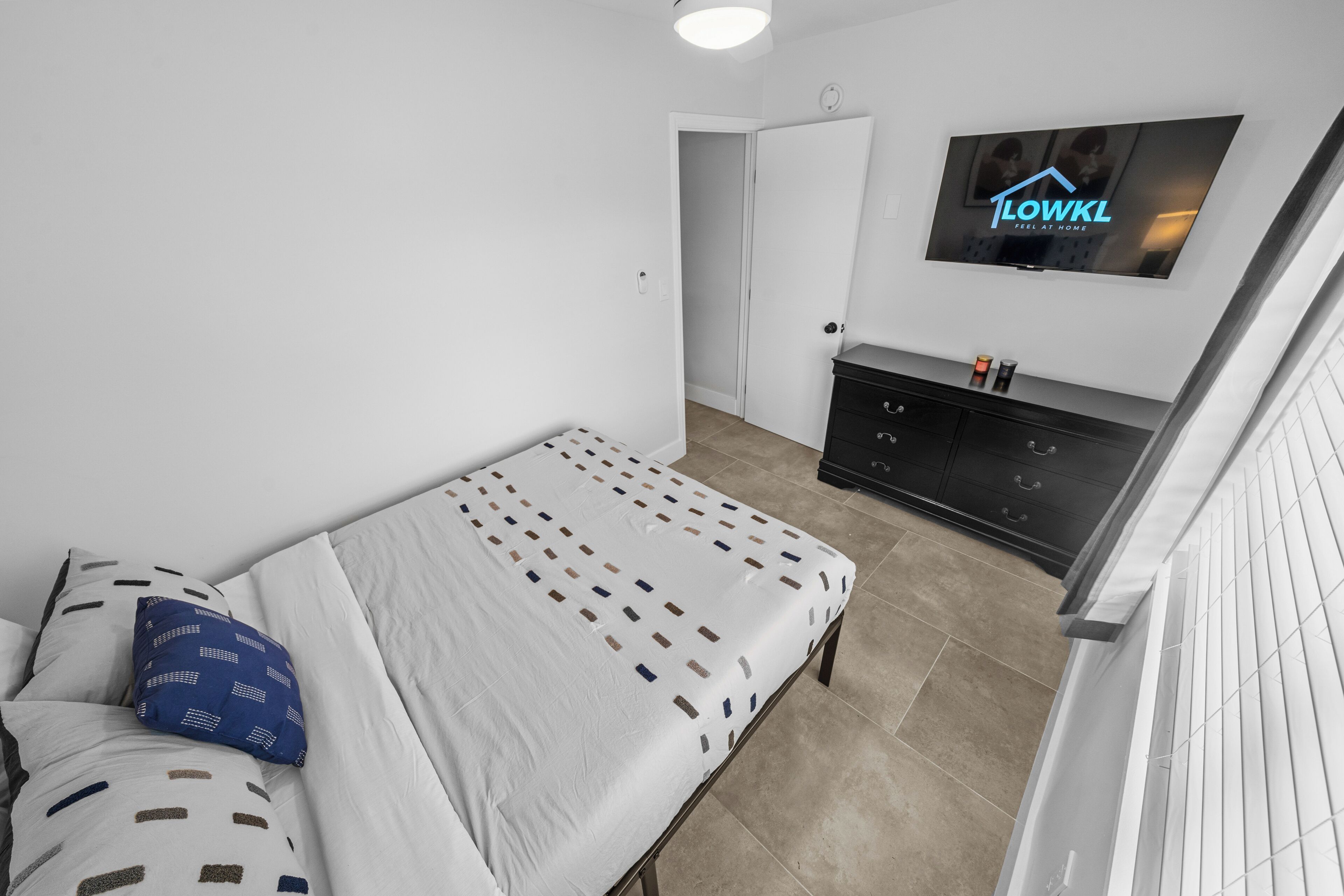 Un dormitorio con cama, televisor montado en la pared y cómoda de color oscuro.