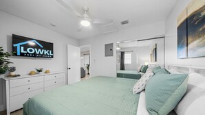 A bedroom with a bed, a ceiling fan, a TV mounted on the wall, and a sign that reads "LOWK'L FEEL AT HOME". - Relaxing 2-Bedroom Apartment w / Pool Access (Fort Lauderdale)