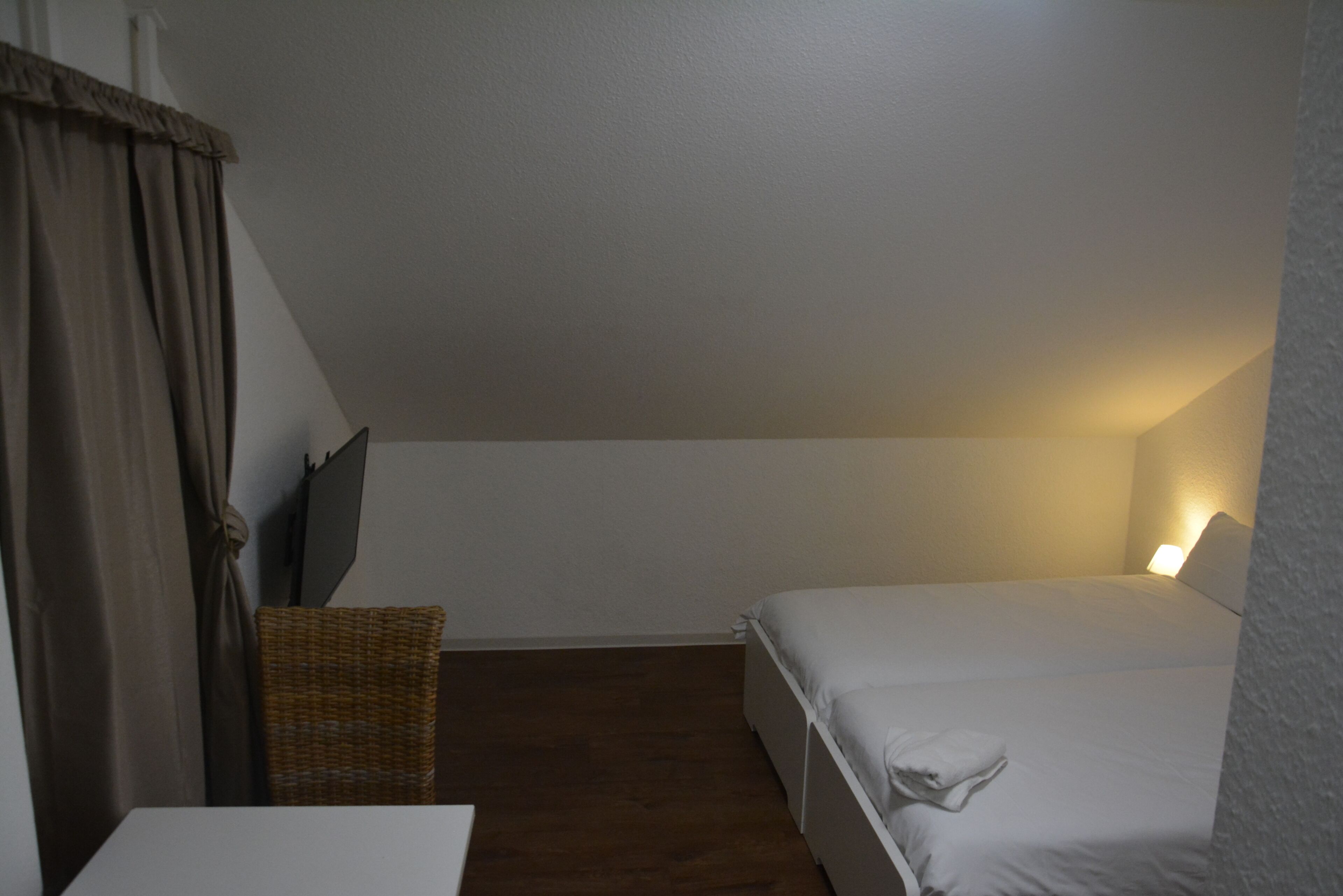 Ein kleiner, schlicht eingerichteter Raum mit einem Bett, einem Sessel und einem Tisch.