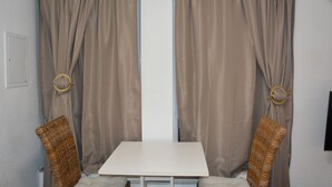 Une pièce avec une table blanche, deux chaises en osier et des rideaux beiges ornés d’anneaux circulaires.