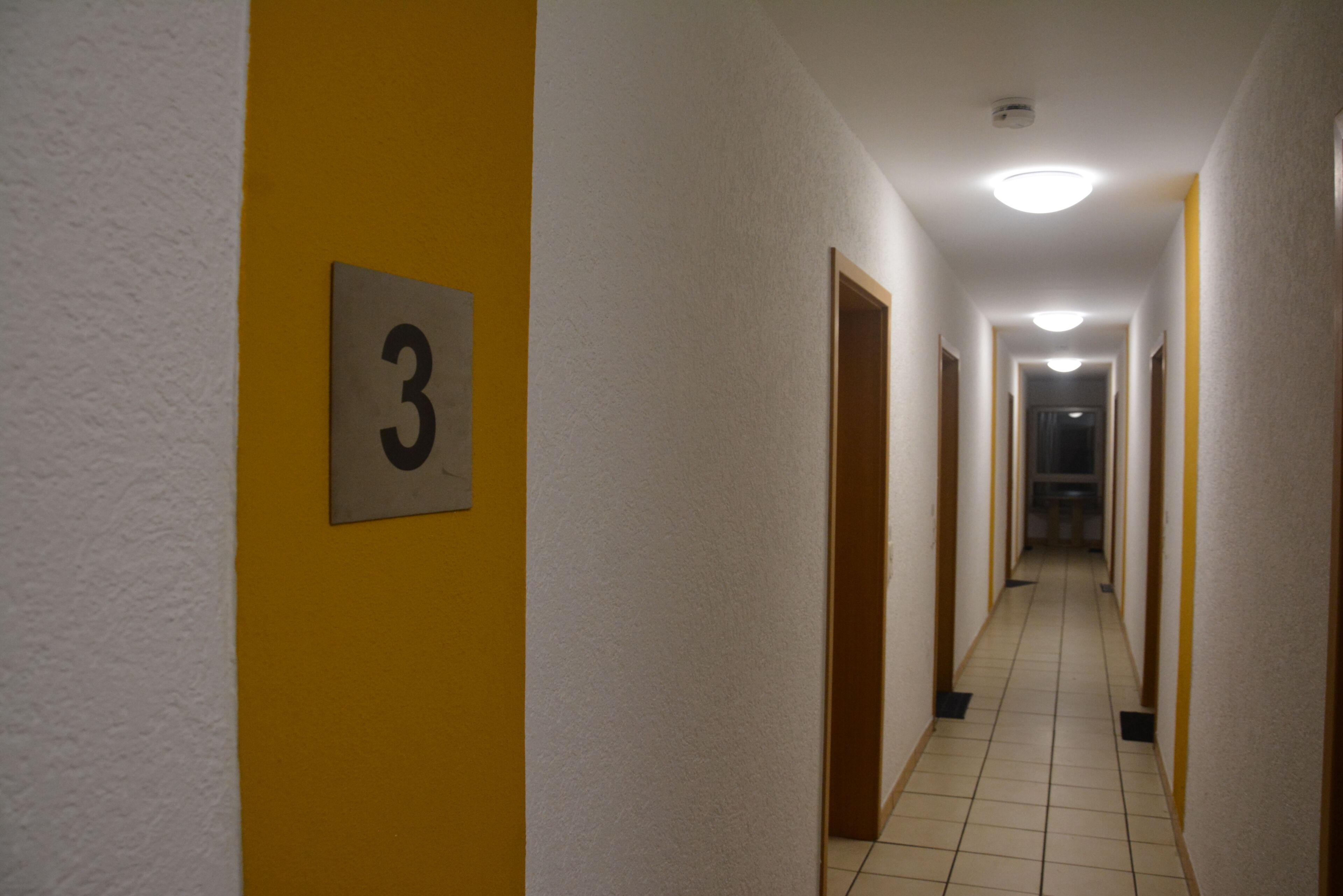Ein Flur mit der Nummer 3 an der Wand, mit Fliesenboden und Türen auf beiden Seiten.