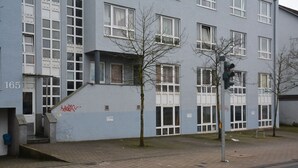 Un immeuble à plusieurs étages, doté d’une façade sobre, portant le numéro 165, et devant lequel se trouve un petit arbre.