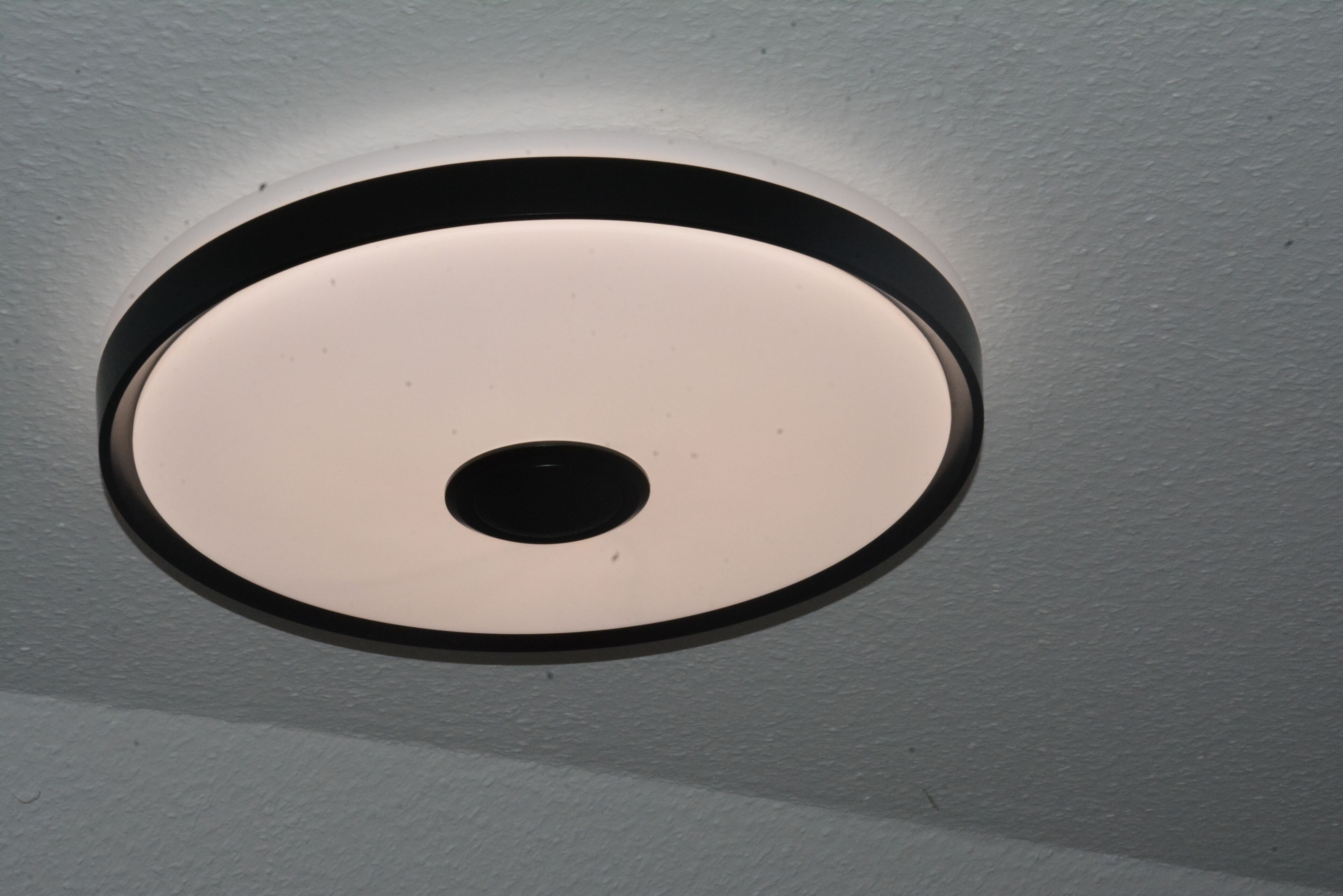 Een ronde plafondlamp met een zwarte stip in het midden.