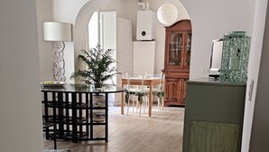 Un espacio habitable amplio con piso de madera, una mesa de comedor con sillas, un mueble verde y una lámpara decorativa.