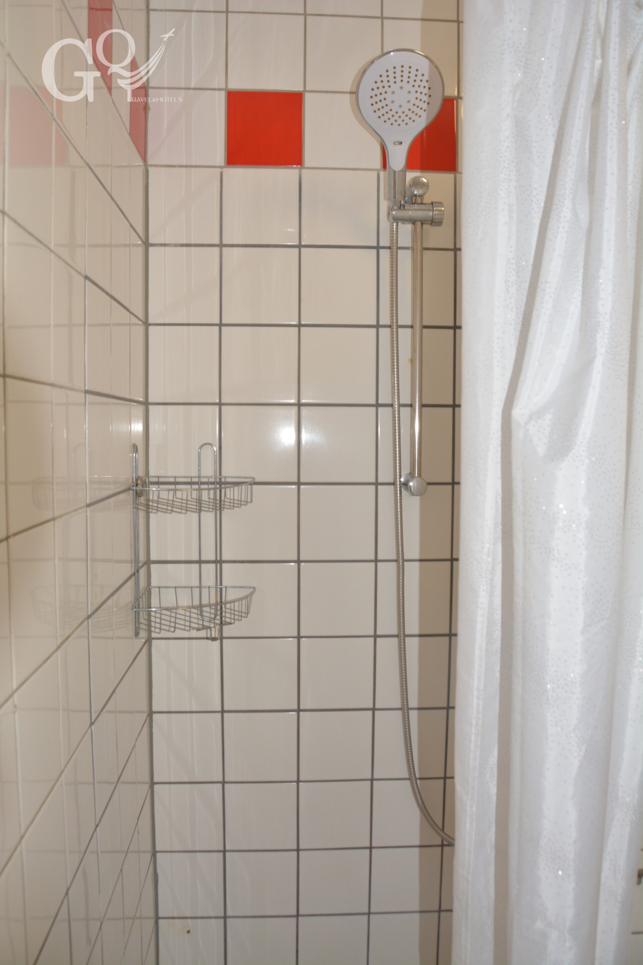 Un espace douche équipé d’un pommeau de douche à main, d’une étagère fixée au mur et d’un mur carrelé agrémenté d’une touche de rouge.