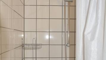 Un espace douche équipé d’un pommeau de douche à main, d’une étagère fixée au mur et d’un mur carrelé agrémenté d’une touche de rouge.