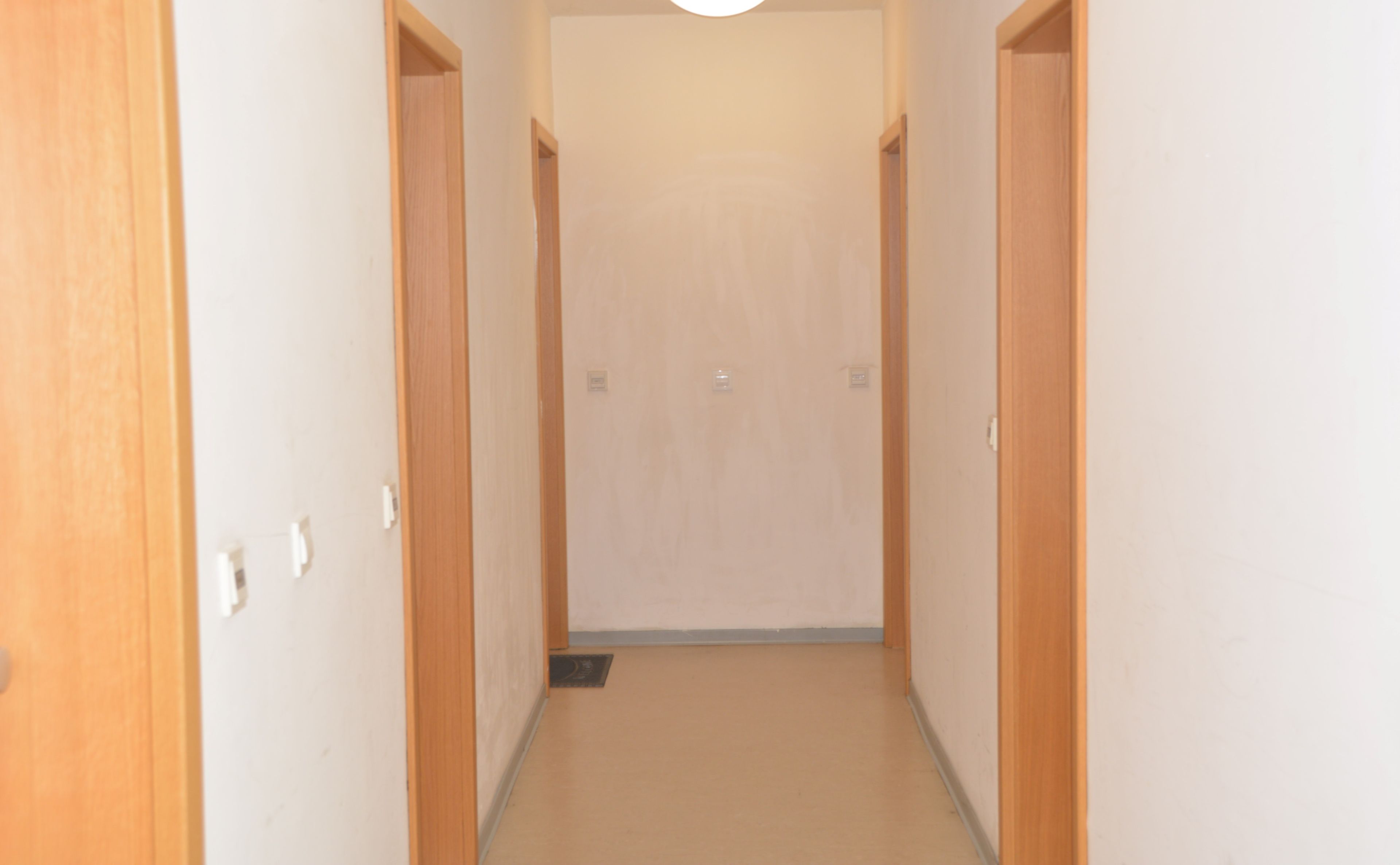 Ein schmaler Korridor mit Holztüren an beiden Seiten und einer Leuchte an der Decke.